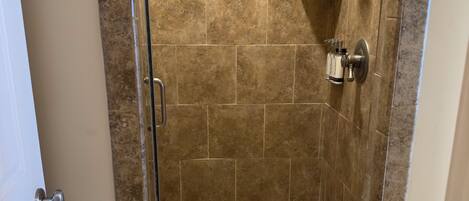 A walk-in shower with a glass door, a white towel on the floor, and a showerhead mounted on the wall.