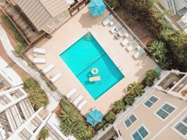 Vista aérea de una piscina rodeada de sillones de descanso y sombrillas, con un bar junto a la piscina y abundante vegetación.