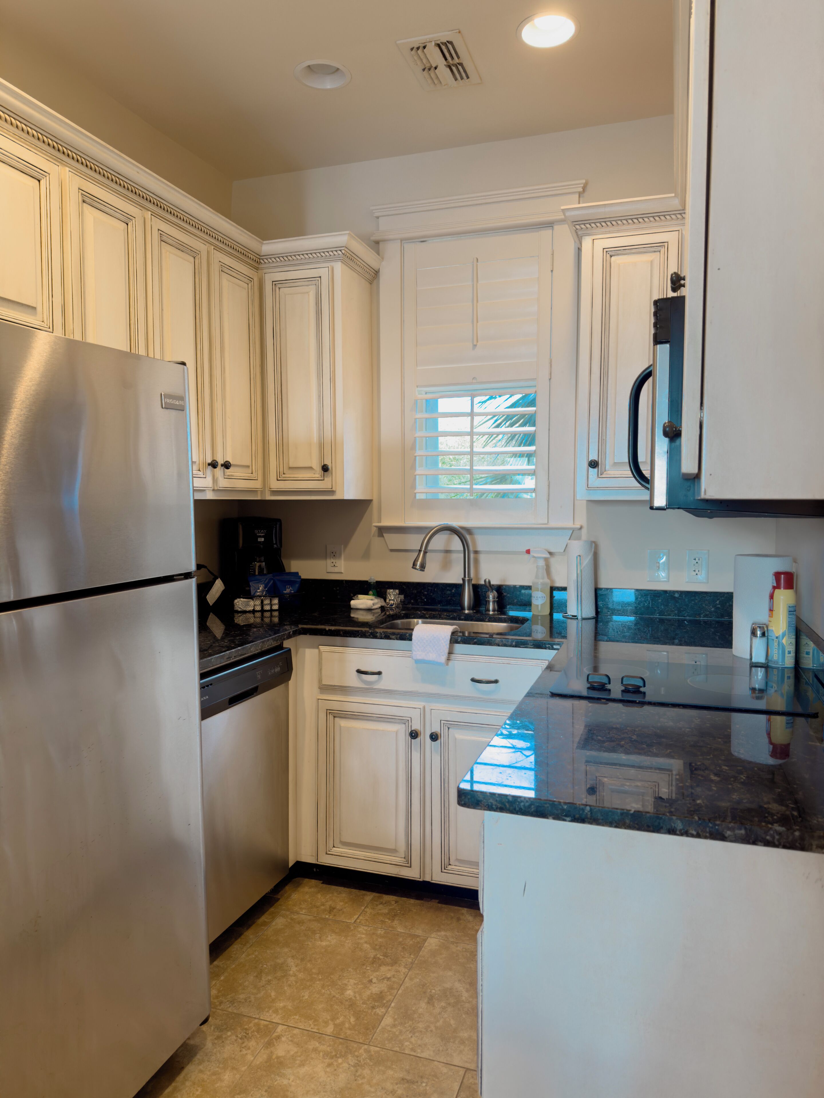 A kitchen with white cabinetry, a stainless steel refrigerator, a built-in oven, a sink, and a window with blinds.