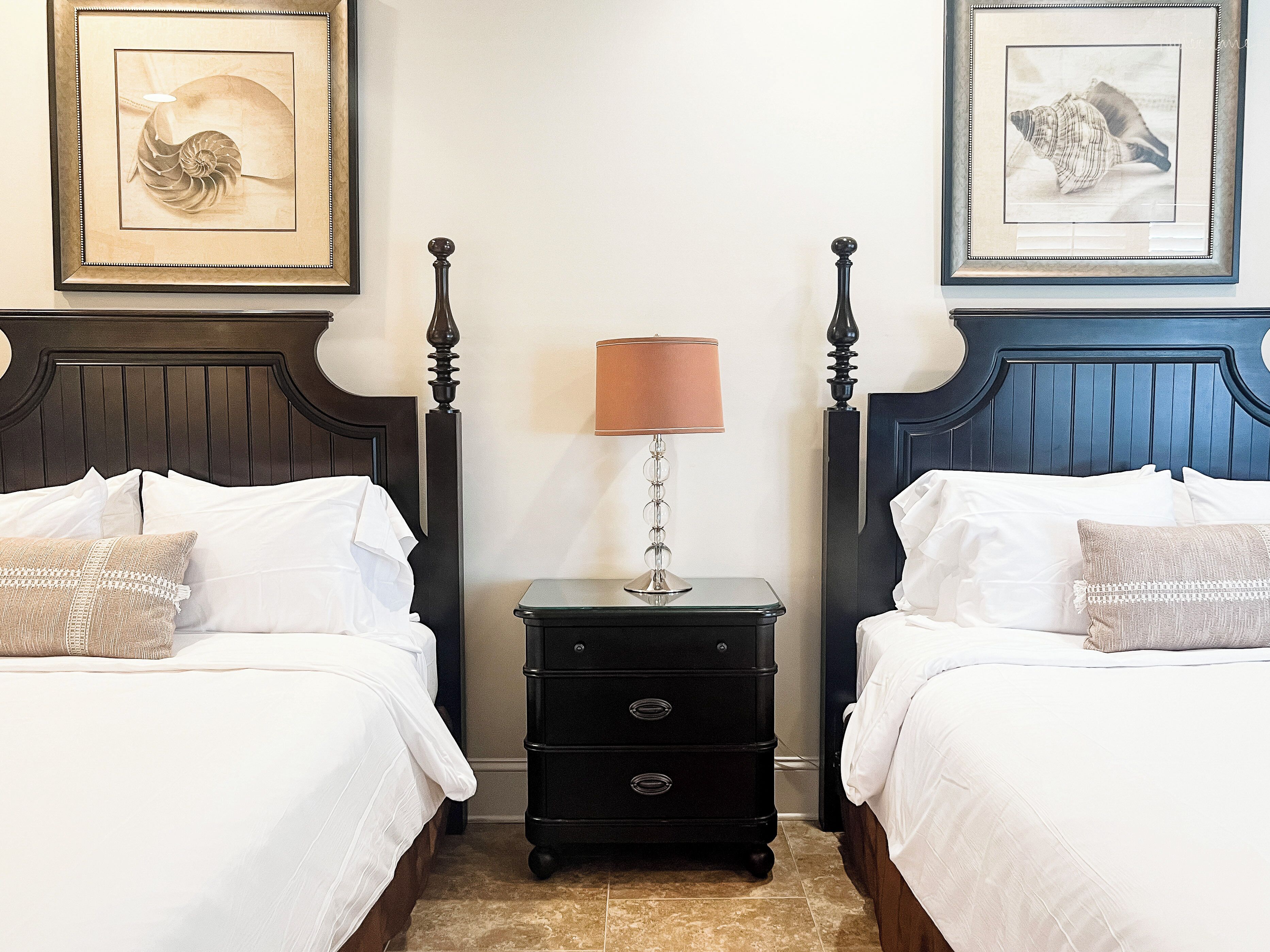 Una habitación de hotel con dos camas, una mesita de noche con lámpara y cuadros en las paredes.