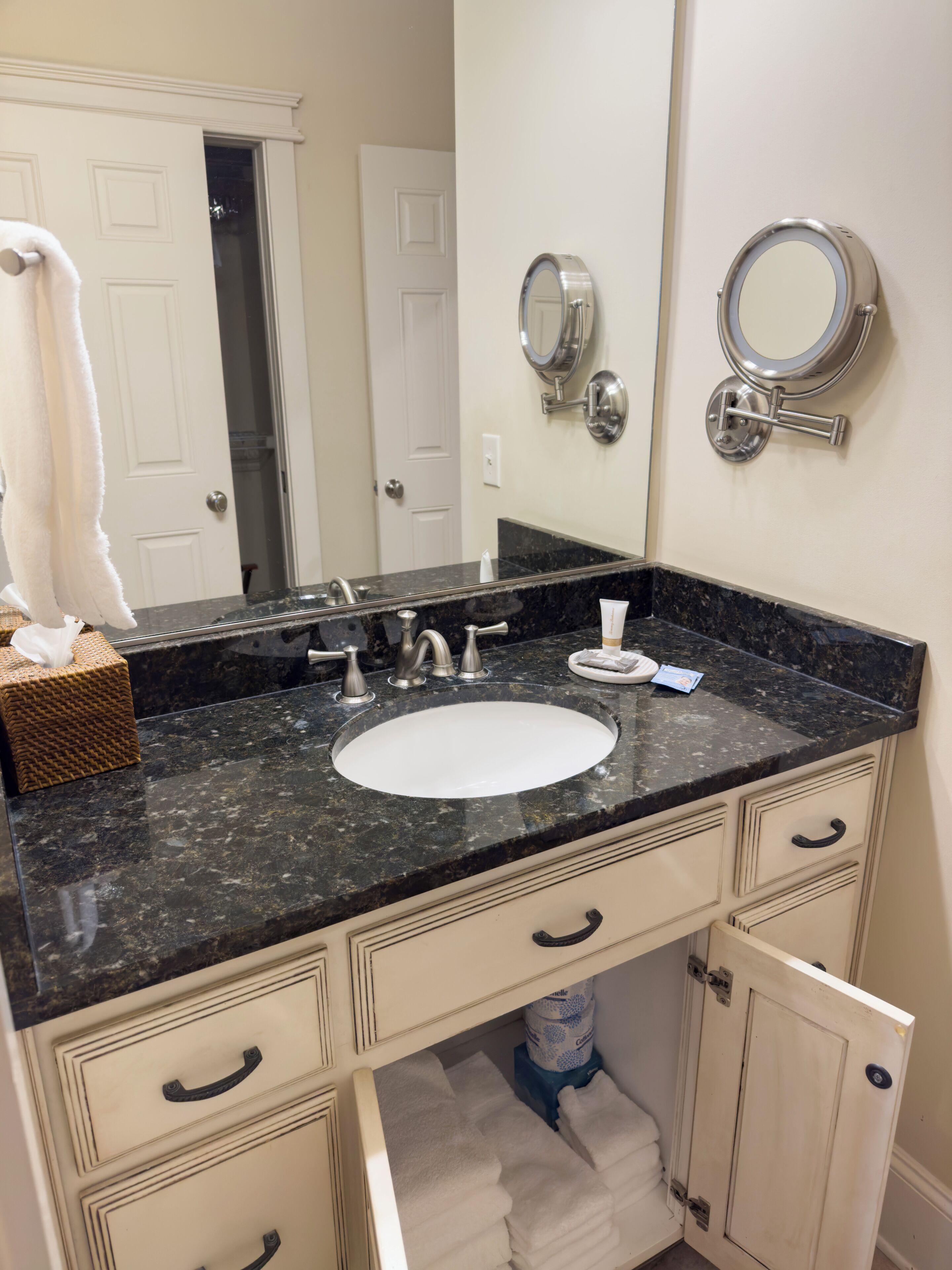 A bathroom with a black granite countertop, white sink, and two wall-mounted mirrors. There are white towels and a tissue box on the counter.