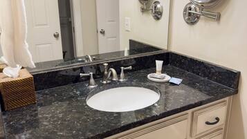 A bathroom with a black granite countertop, white sink, and two wall-mounted mirrors. There are white towels and a tissue box on the counter.