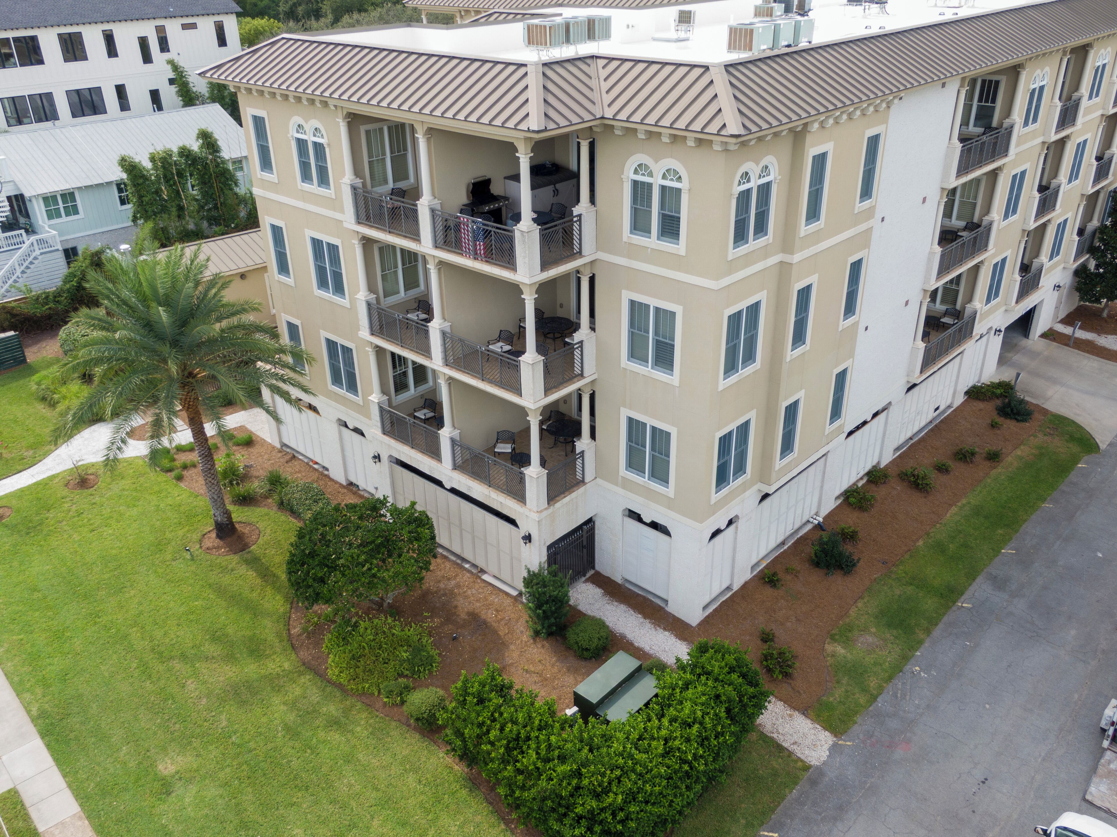 A multi-story building with balconies, a palm tree, and a well-maintained lawn.