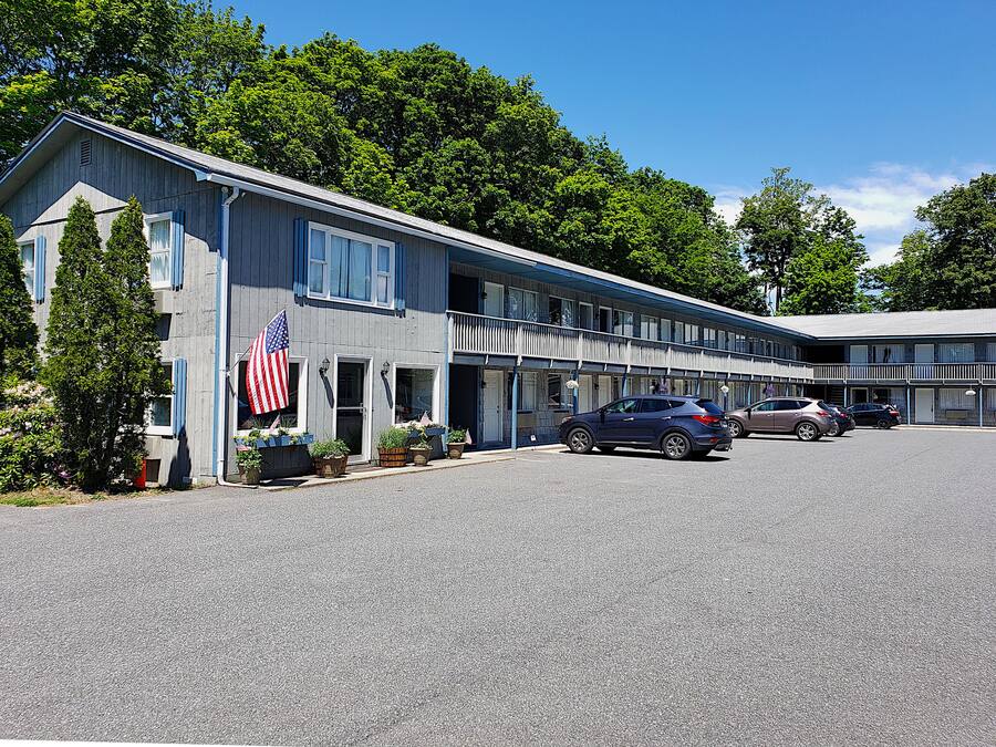 Um motel com estrutura em dois andares, estacionamento e uma fileira de carros estacionados na frente.