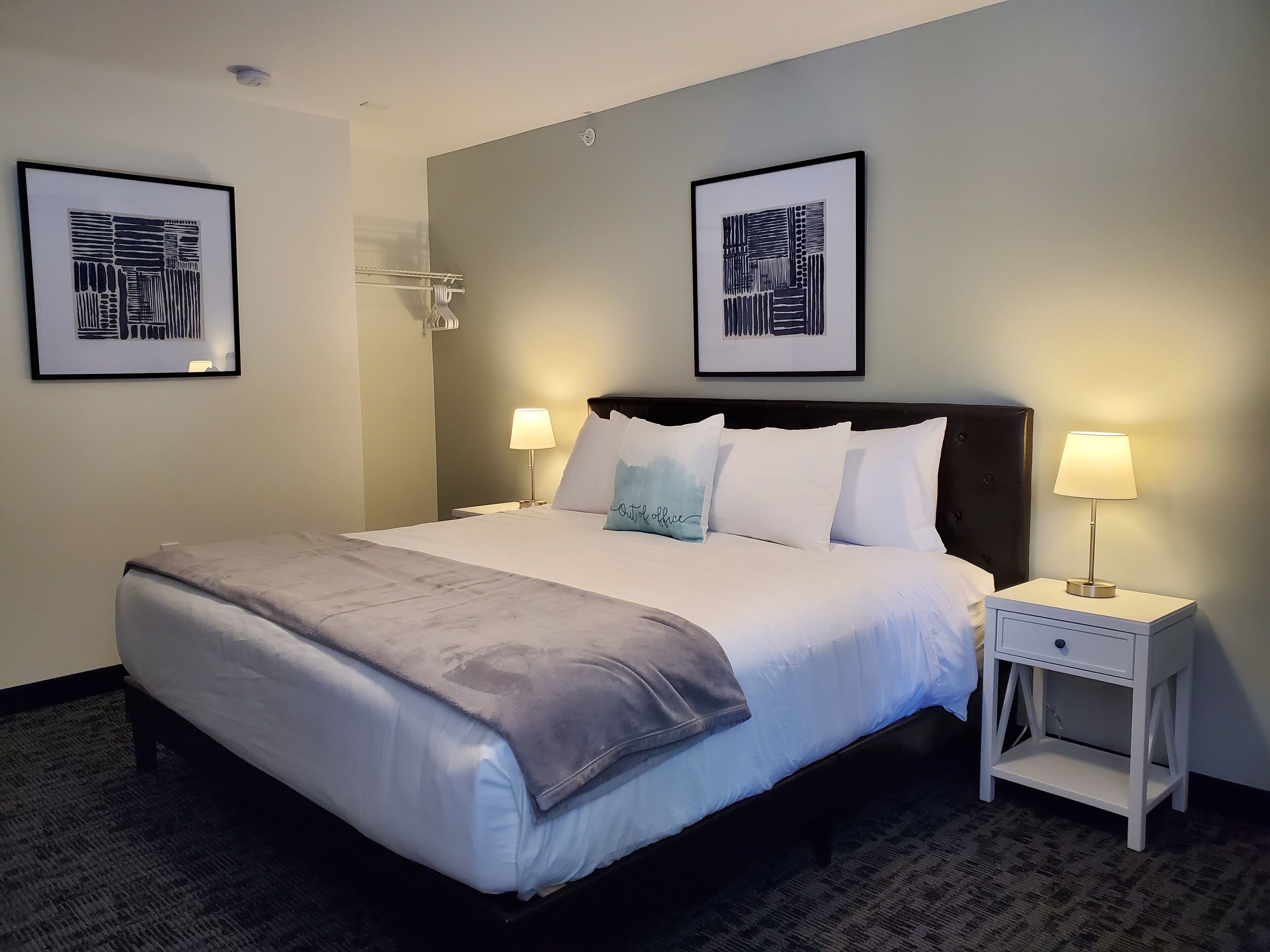 A neatly made bed with a grey blanket, two bedside lamps, and two framed artworks on the wall.