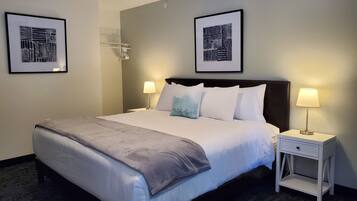 A neatly made bed with a grey blanket, two bedside lamps, and two framed artworks on the wall.