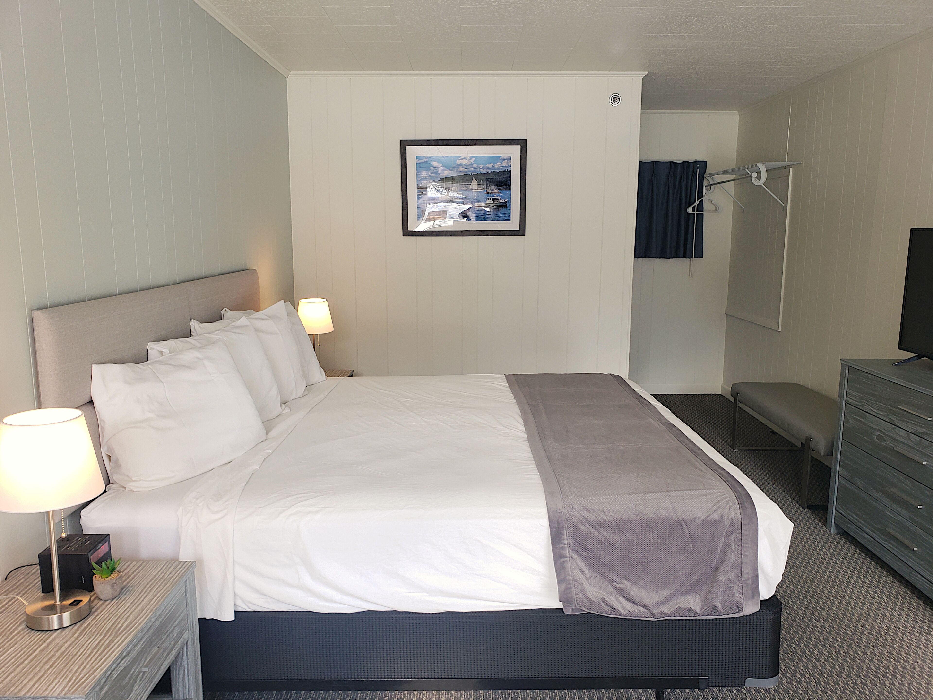 A hotel room with a bed, bedside lamps, a framed picture on the wall, a dresser, and a television.