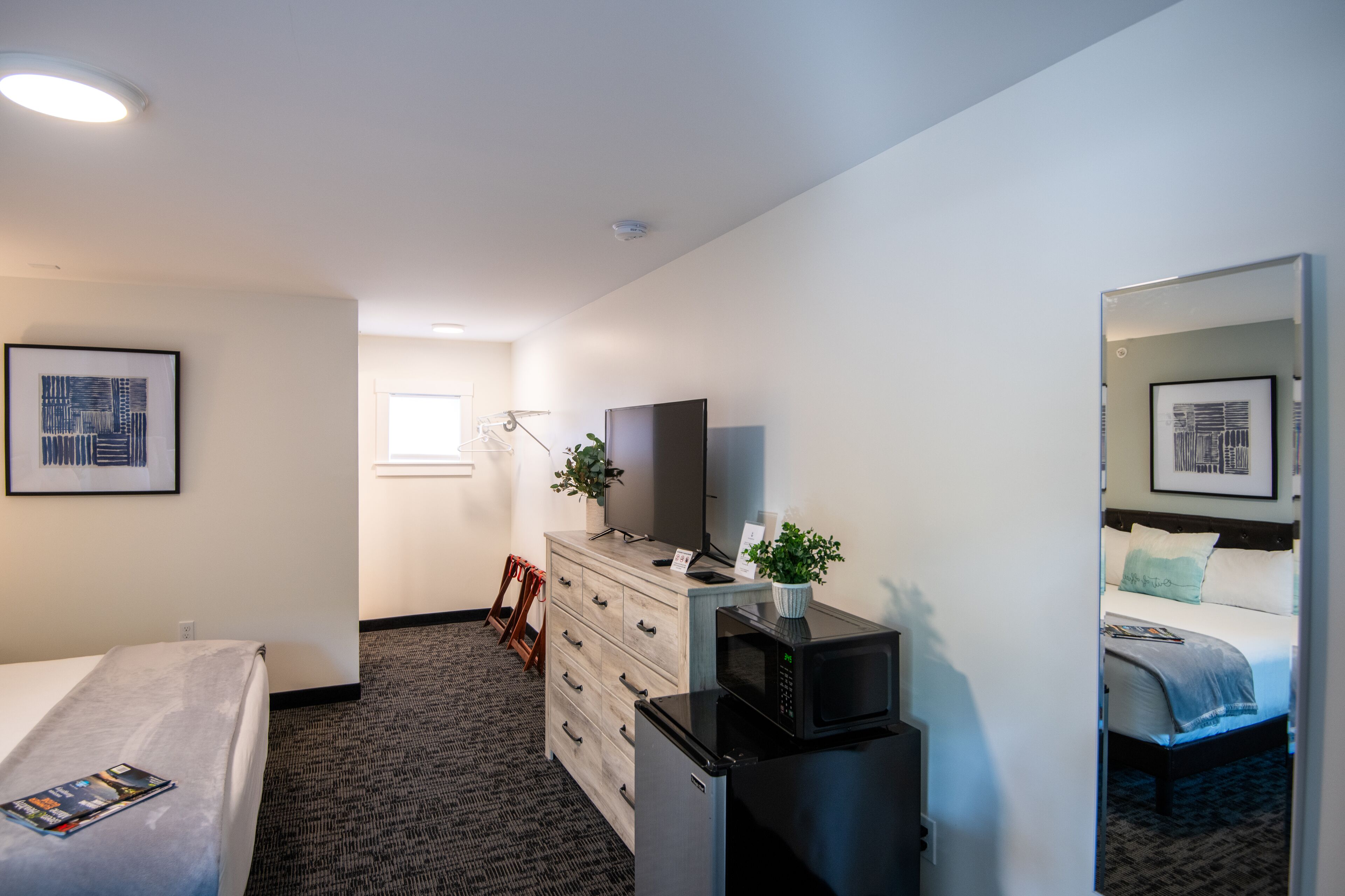 A hotel room with a bed, a dresser, a microwave, a TV, and a mirror.