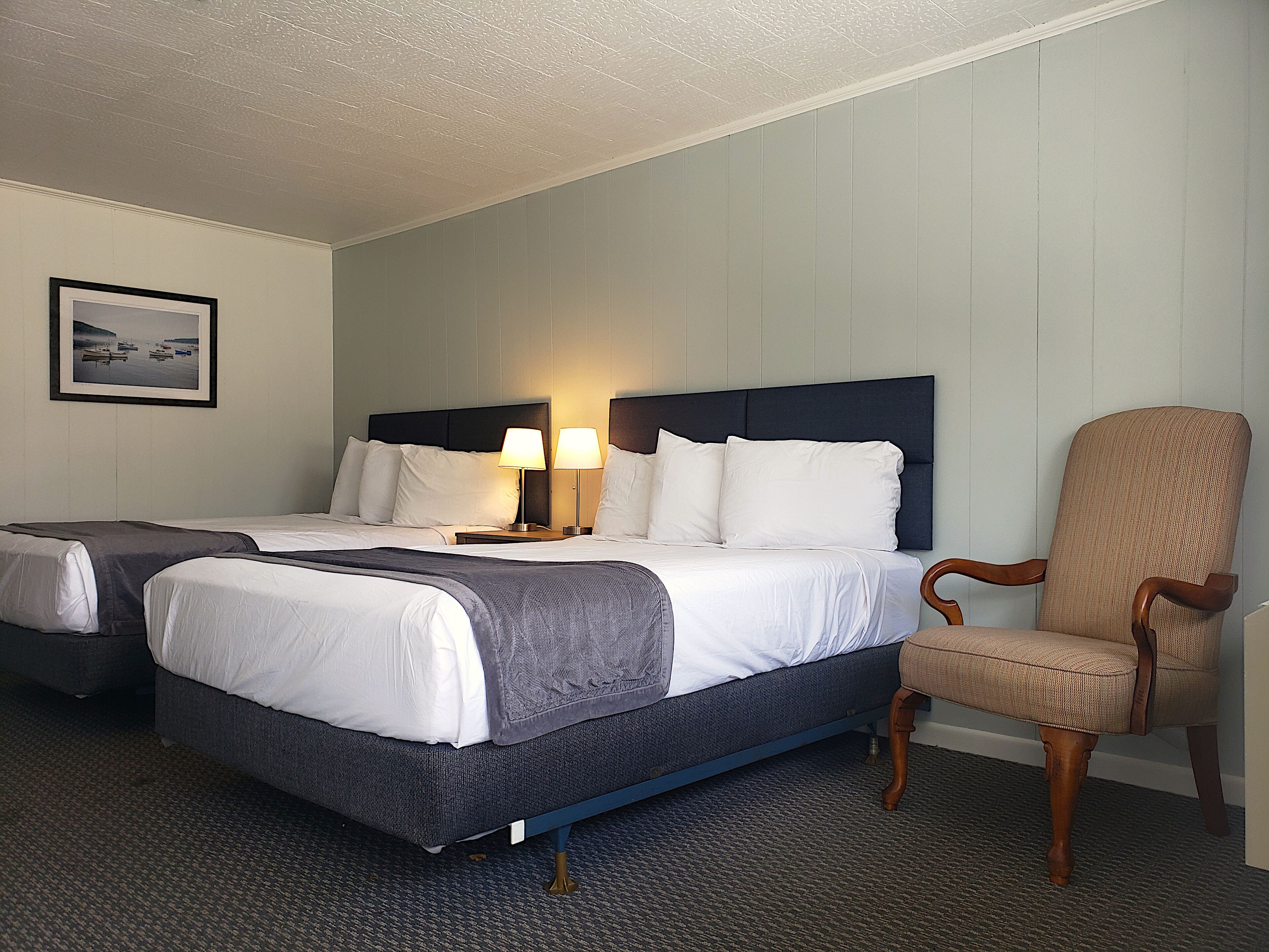 A hotel room with two beds, a chair, and a framed picture on the wall.