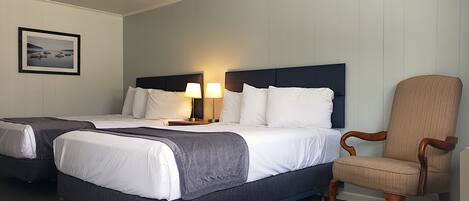 A hotel room with two beds, a chair, and a framed picture on the wall.