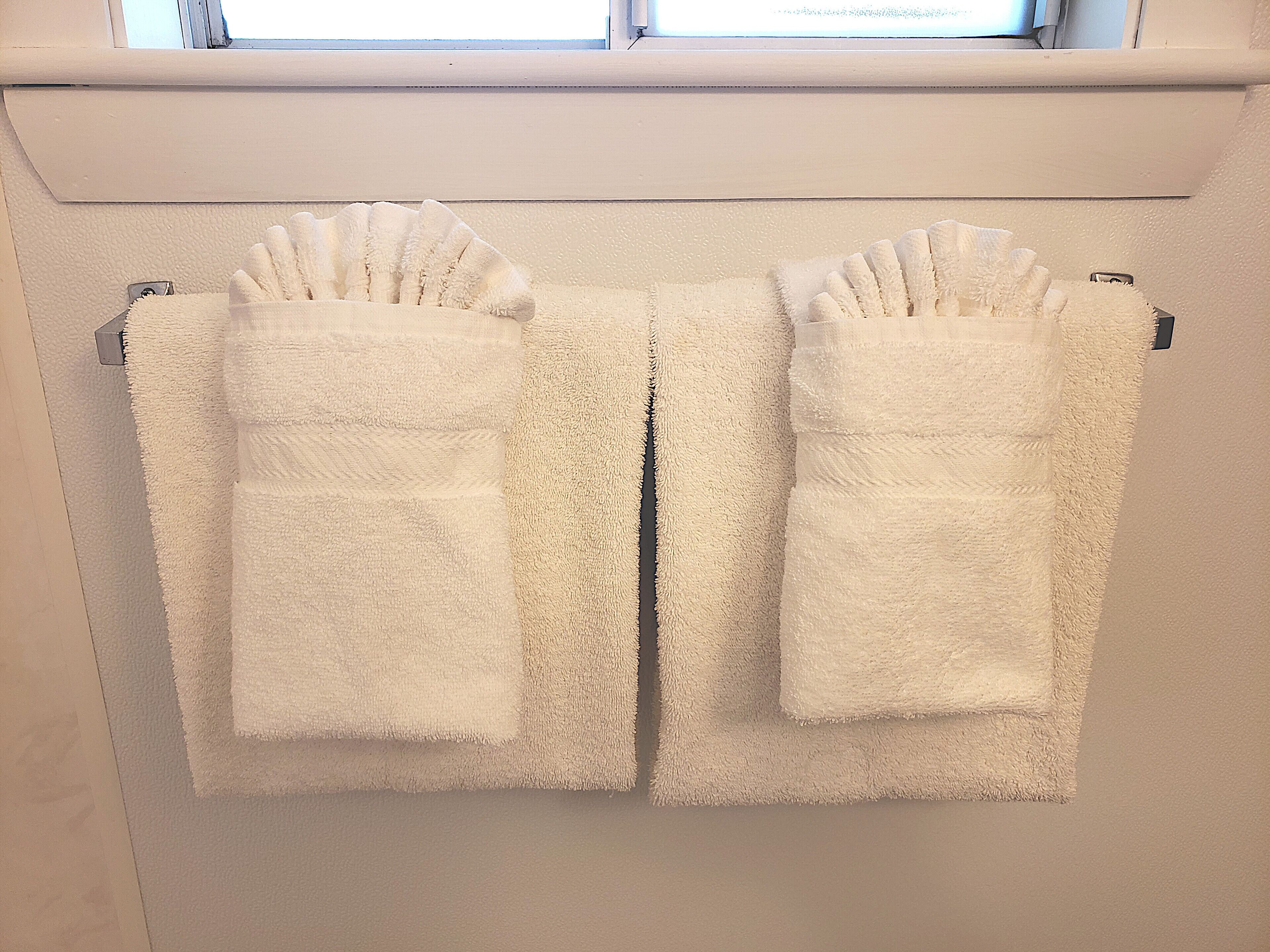A pair of white towels with pockets hanging on a wall-mounted towel rack.