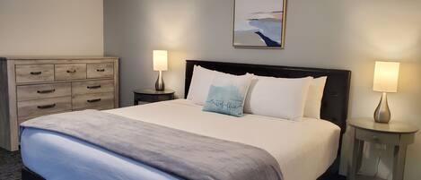 A hotel room with a large bed, two bedside tables with lamps, a dresser, and a painting on the wall.