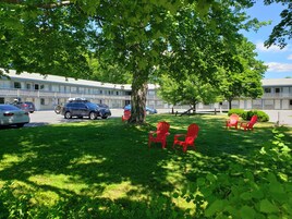 A motel with a parking lot, several cars, and red Adirondack chairs in the grassy area.