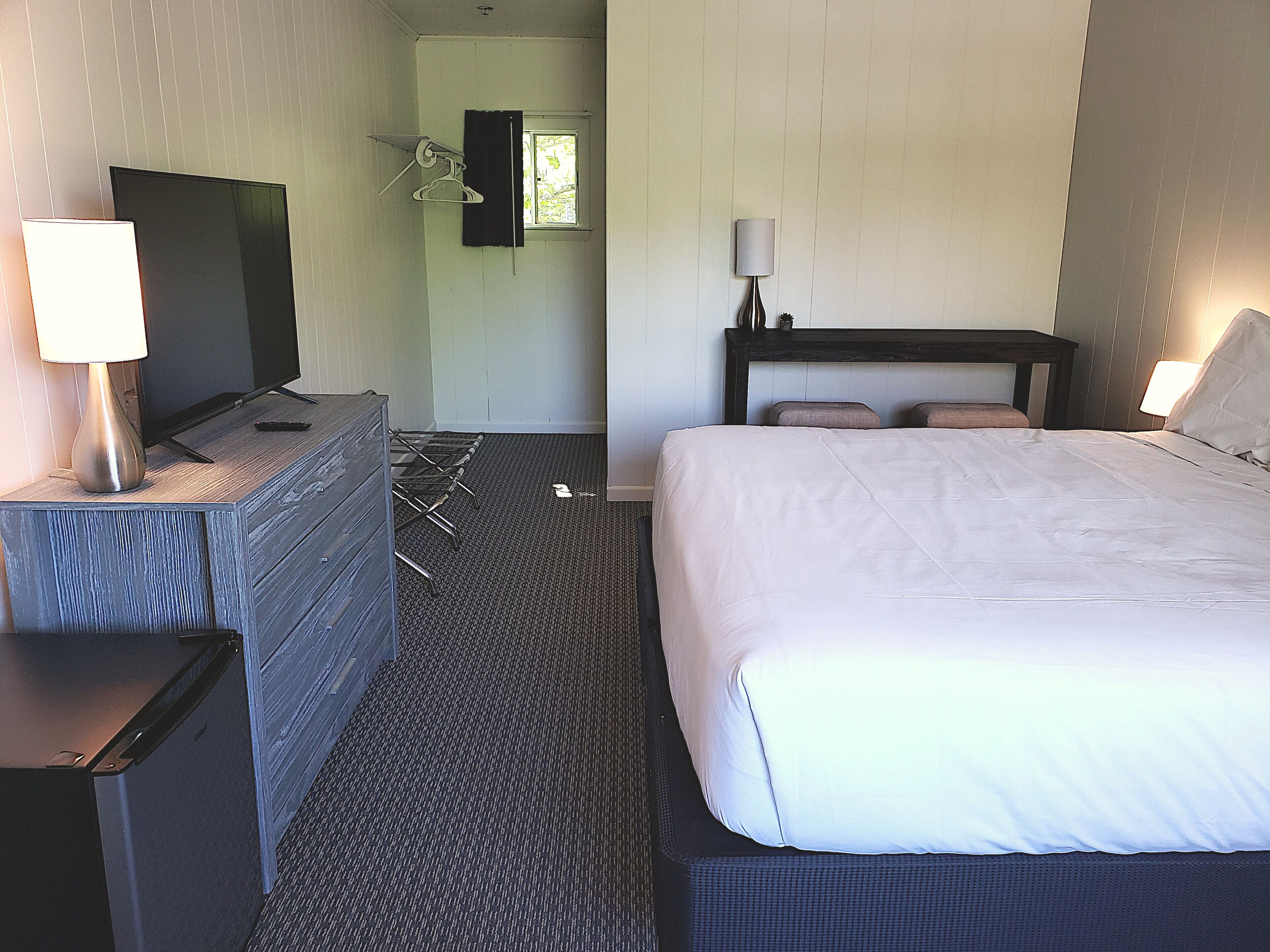 A hotel room with a bed, a TV, a dresser, and a window.
