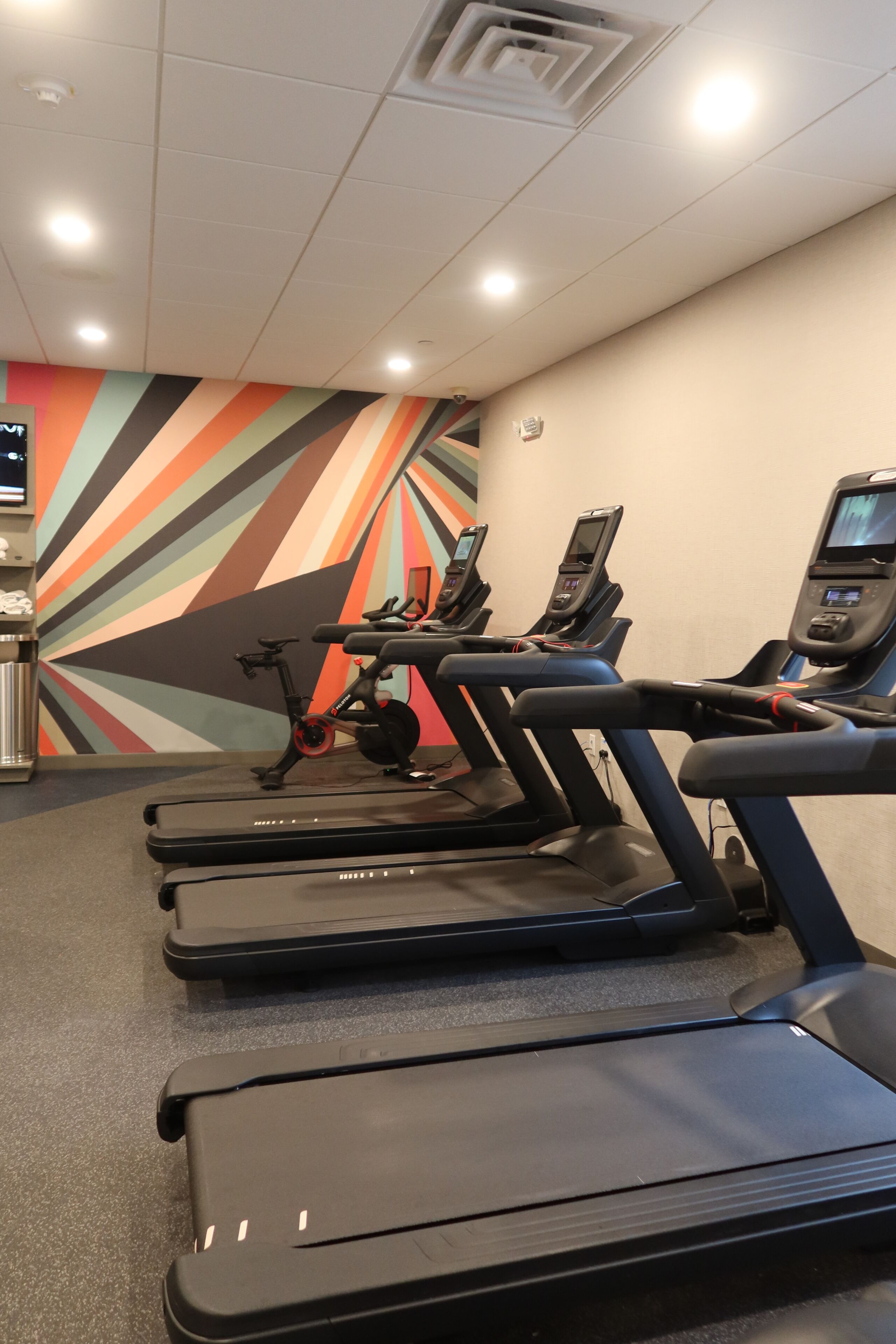 Et fitnesscenter med løbebånd, træningscykler og en farverig væg.