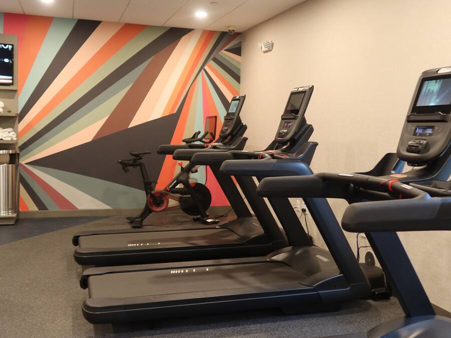 Et fitnesscenter med løbebånd, træningscykler og en farverig væg.