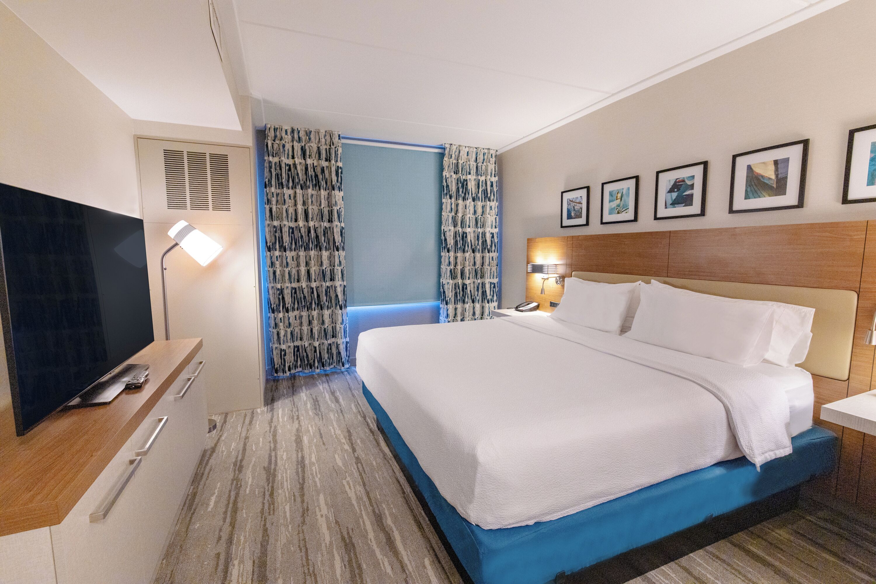 Une chambre d’hôtel avec un grand lit, un téléviseur à écran plat, un bureau avec une lampe et un mur orné de tableaux.