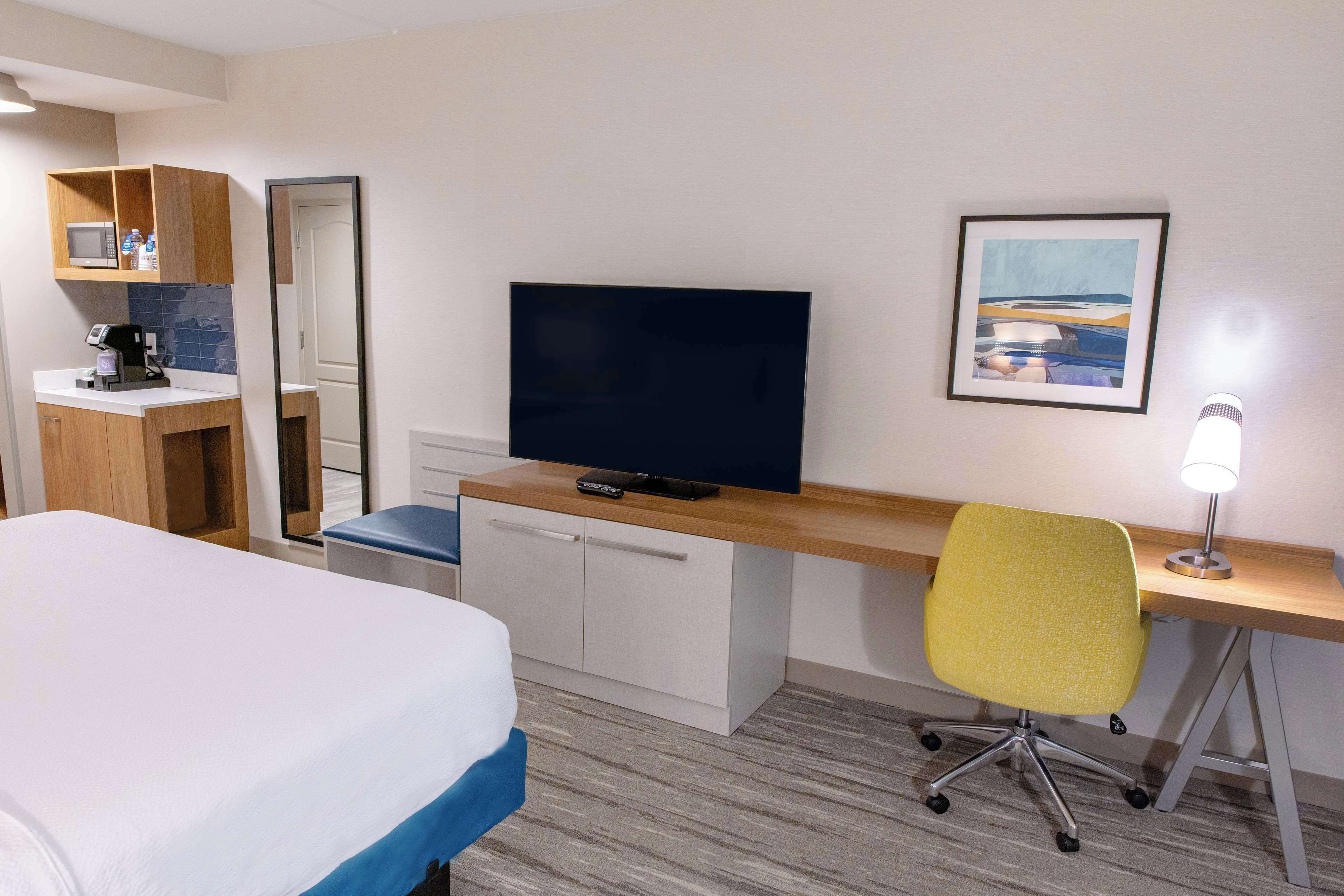 Una camera d'albergo con un letto, una scrivania con una sedia, una televisione, una macchina del caffè e un quadro appeso al muro.