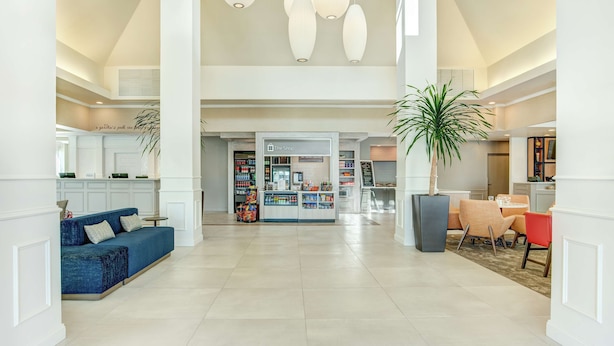 Een ruime lobby met een blauwe bank, een kleine winkel en een eetgedeelte met stoelen.