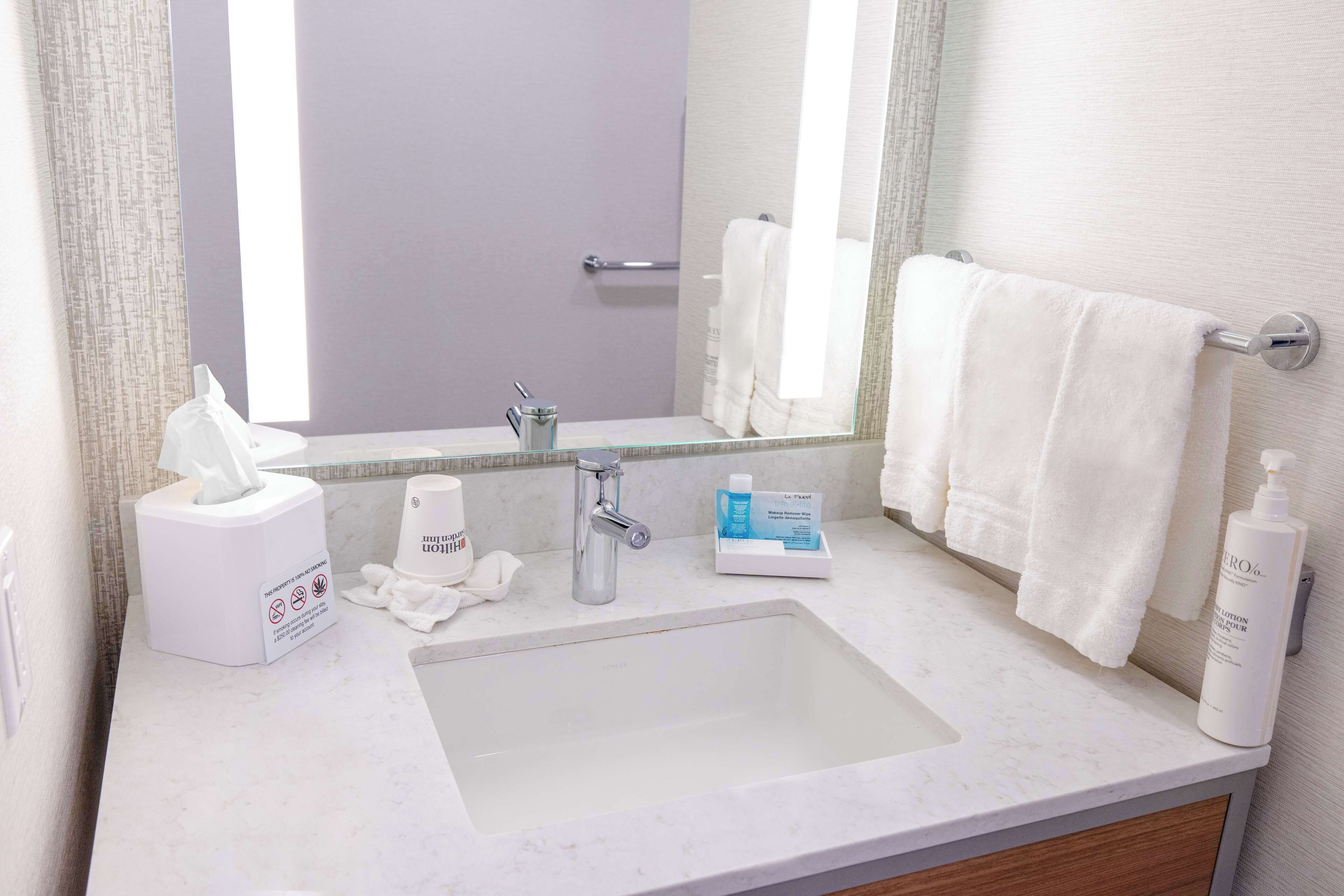 A bathroom with a sink, mirror, towel rack, and toiletries.