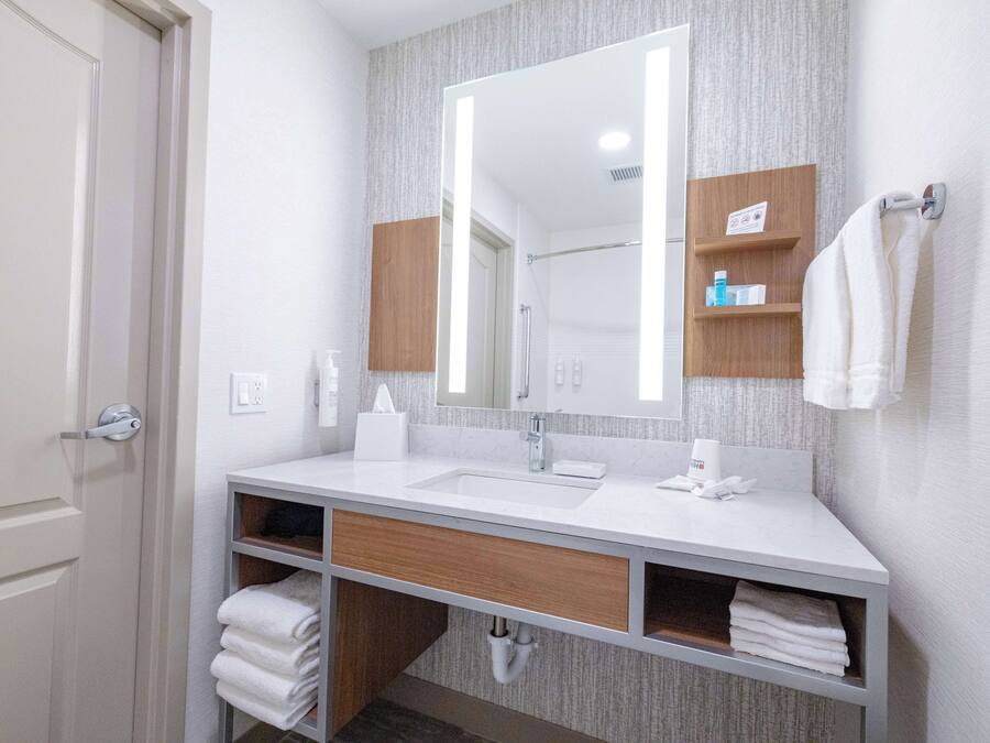 A modern bathroom with a white sink, a large mirror, and wooden shelves.