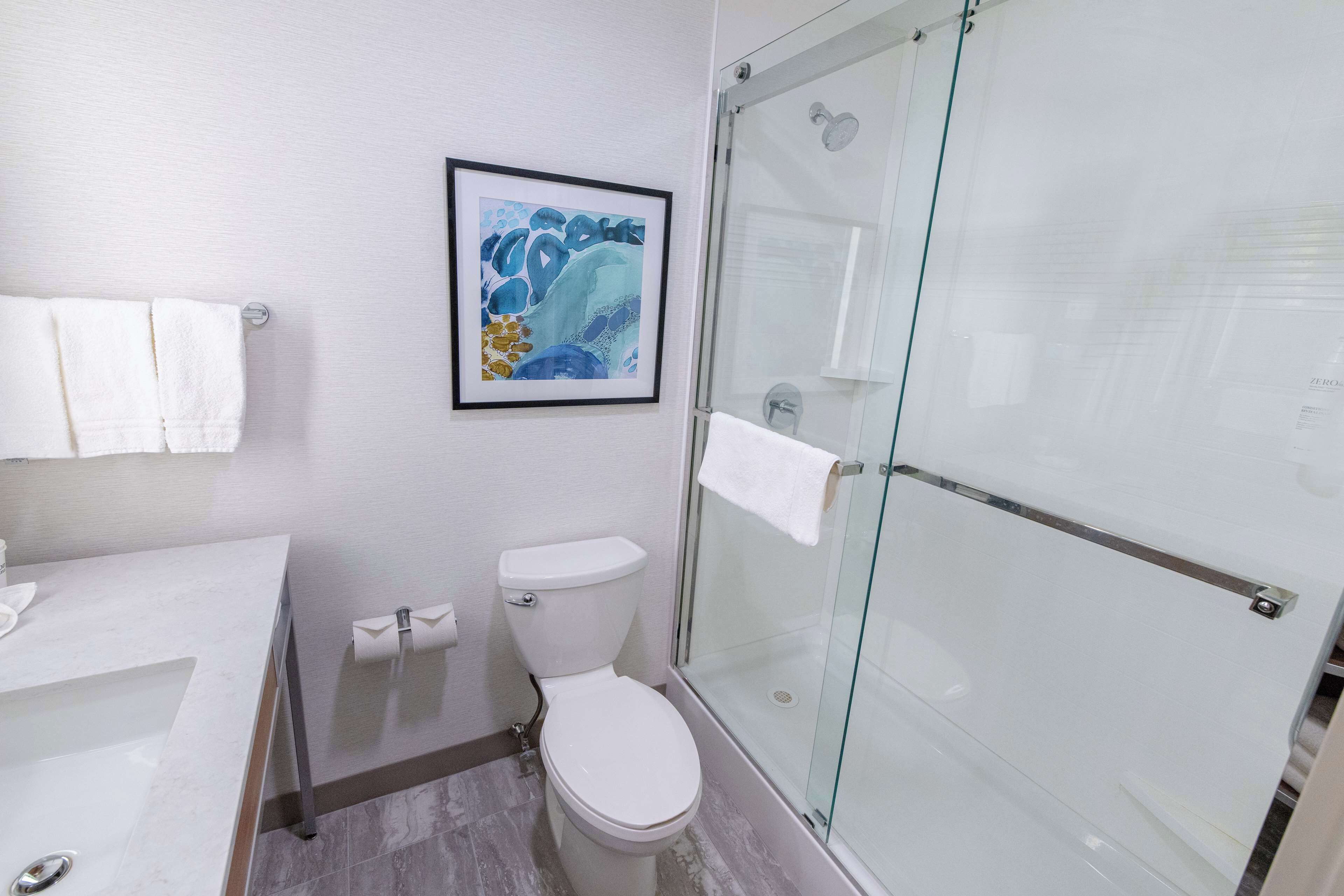 Une salle de bain comprenant des toilettes, un lavabo et une douche fermée par une paroi de verre.