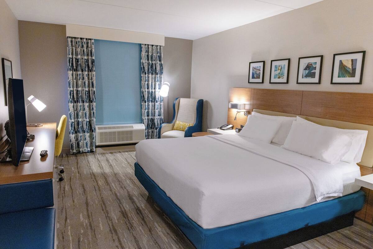 Hotelkamer met een groot bed, een bureau met computer, een stoel, een bureaulamp, een tv aan de muur en een raam met gordijnen.