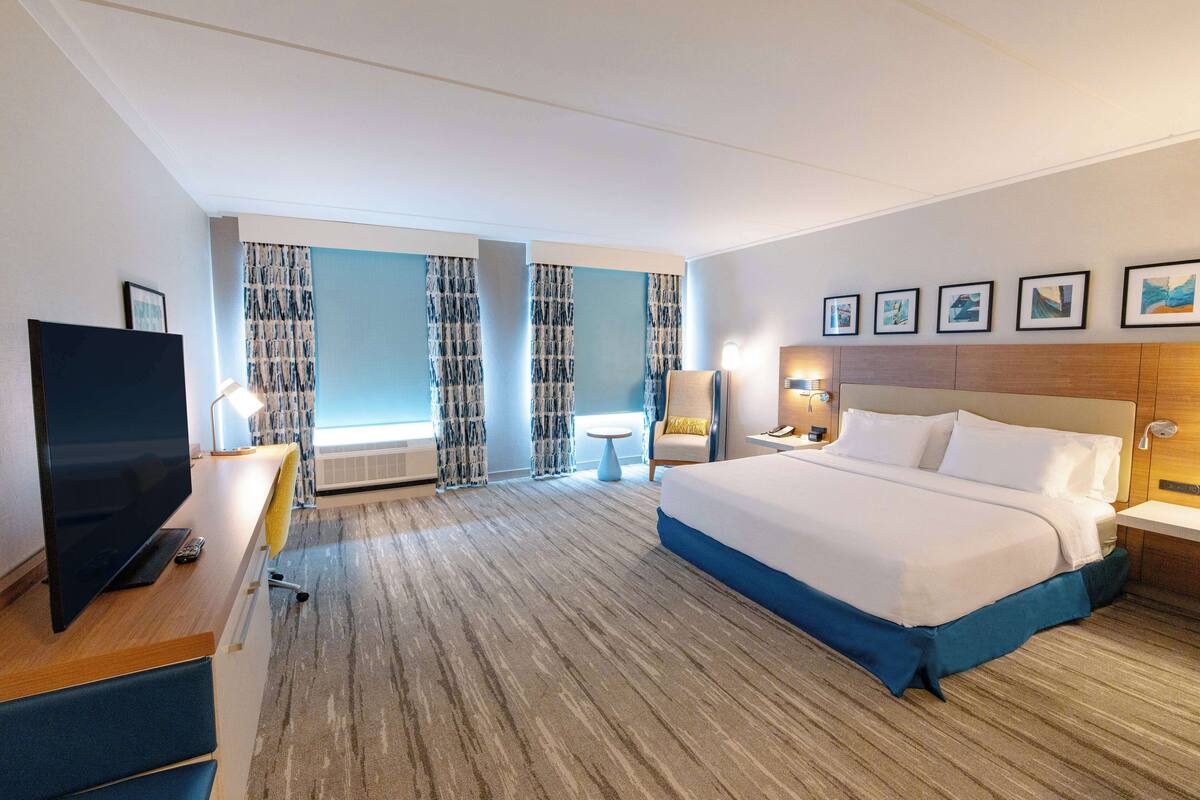 Hotelkamer met een groot bed, een bureau met televisie, een stoel, een klein tafeltje en een raam met gordijnen.