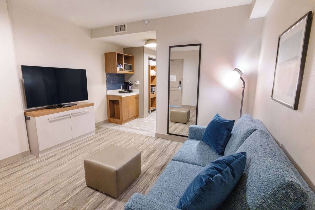 Een moderne woonkamer met een flatscreen televisie, een bank, een salontafel en een keuken in de achtergrond.