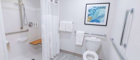 A modern bathroom with a shower, toilet, and handrails.