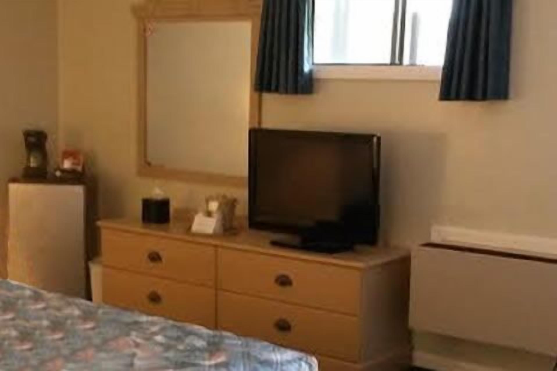 Quarto com cama, penteadeira, televisão e janela com cortinas.