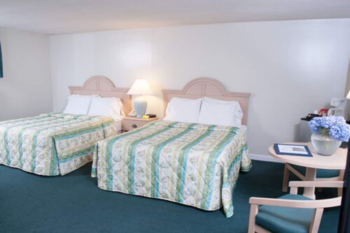 A hotel room with two beds, a small table, a chair, and a lamp.