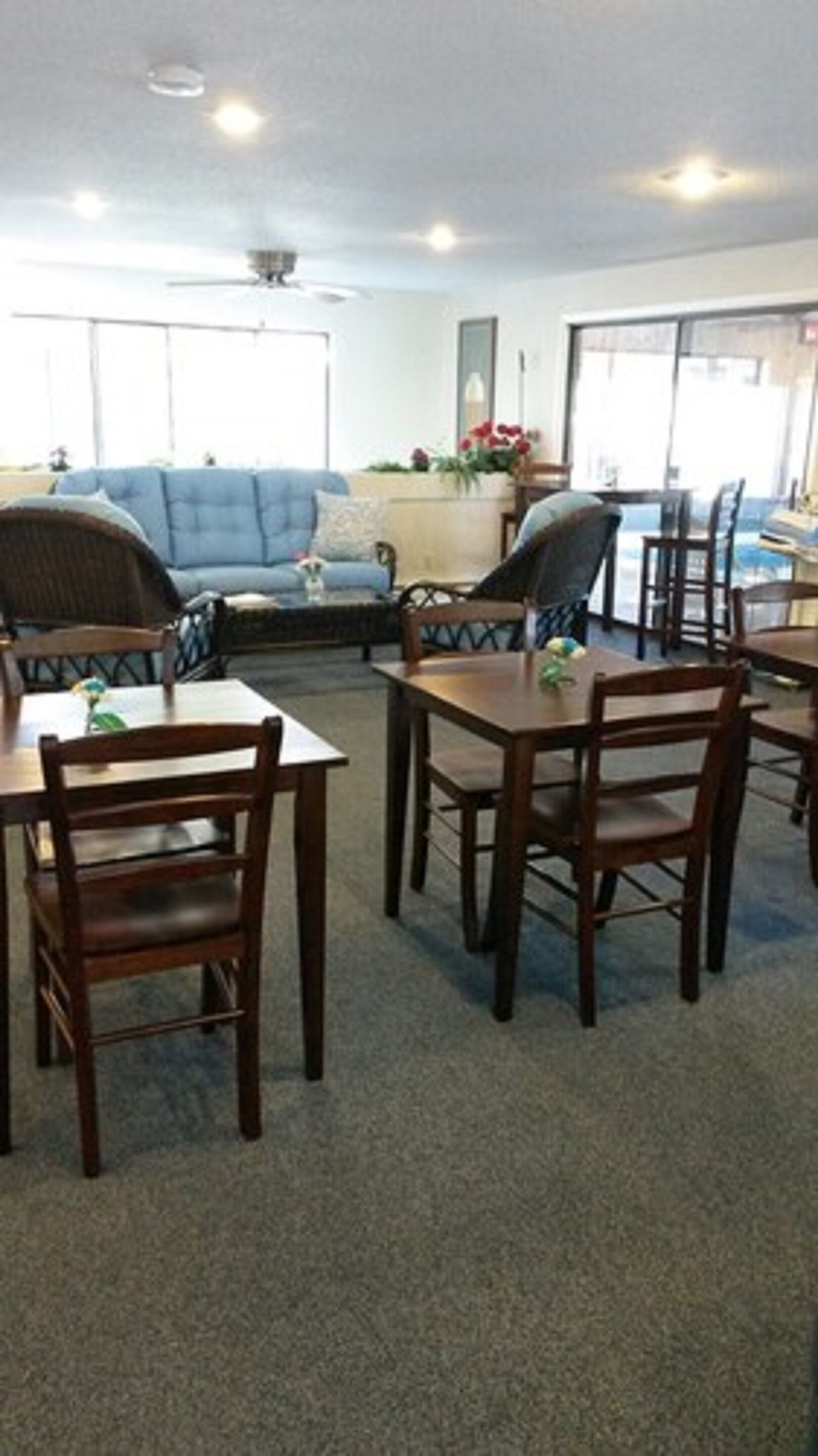 A dining area with wooden tables and chairs, a blue sofa, and a large window with a view.