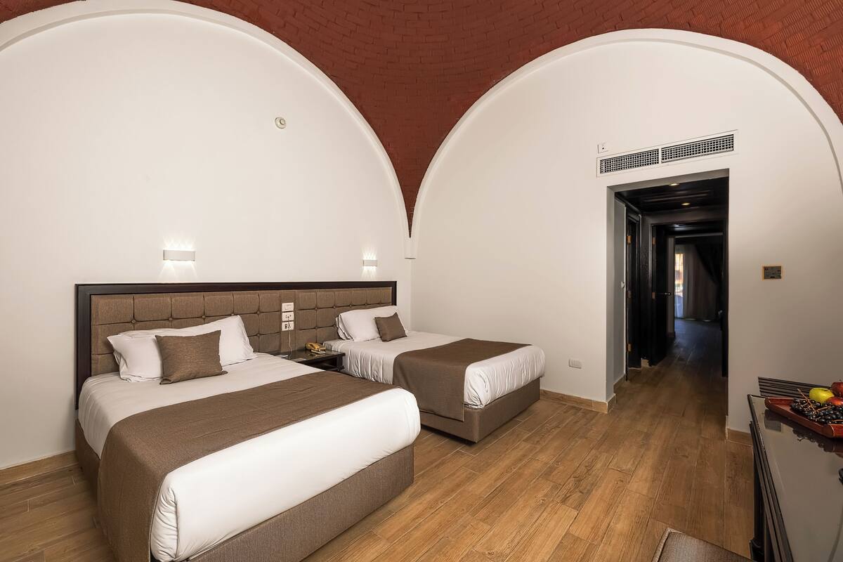 A hotel room with two beds, a wooden floor, and a brick ceiling.