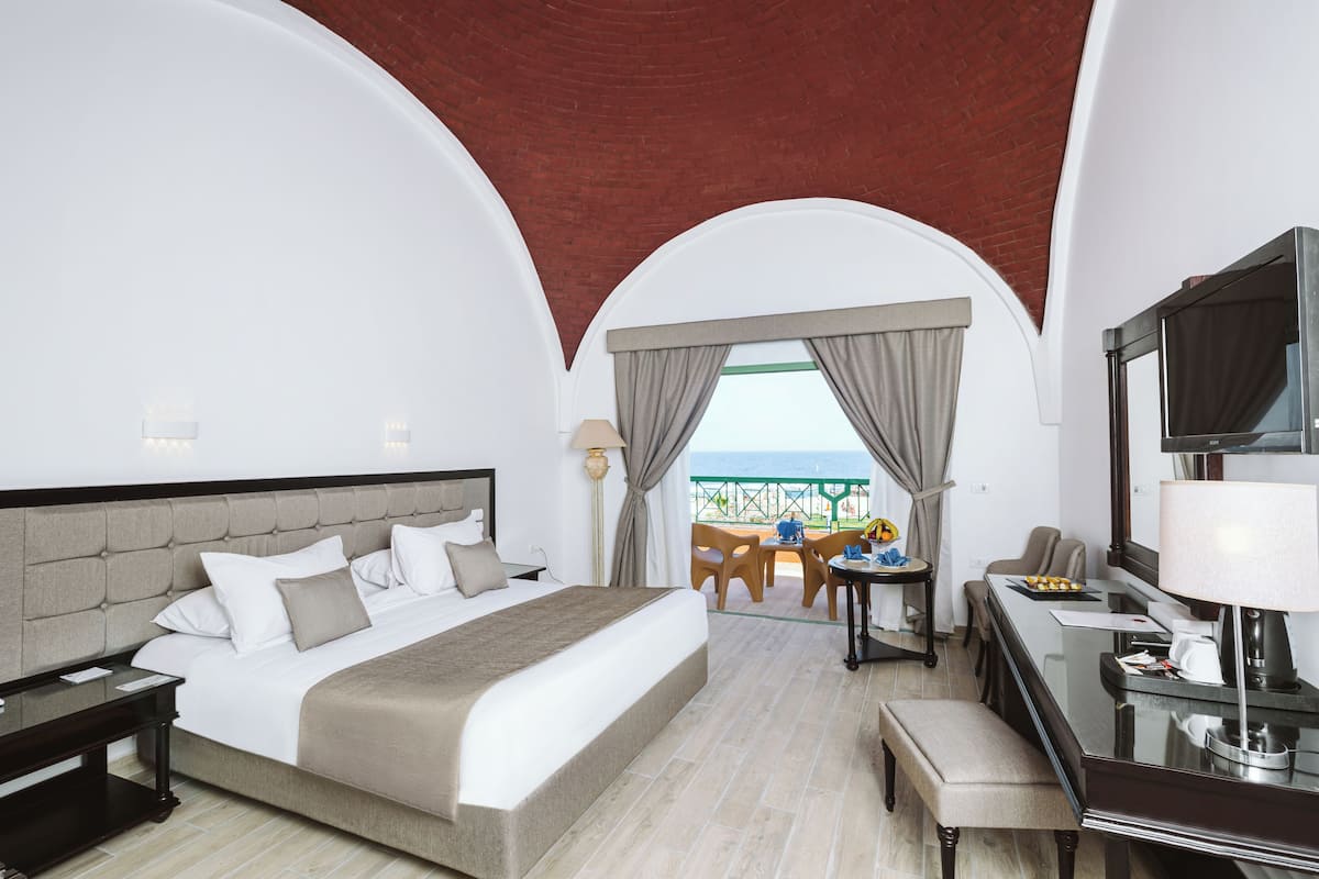 A hotel room with a large bed, a desk, a chair, a TV, and a balcony with a view.