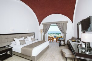 Habitación de hotel con una cama grande, un escritorio, una silla, un televisor y un balcón con vistas.