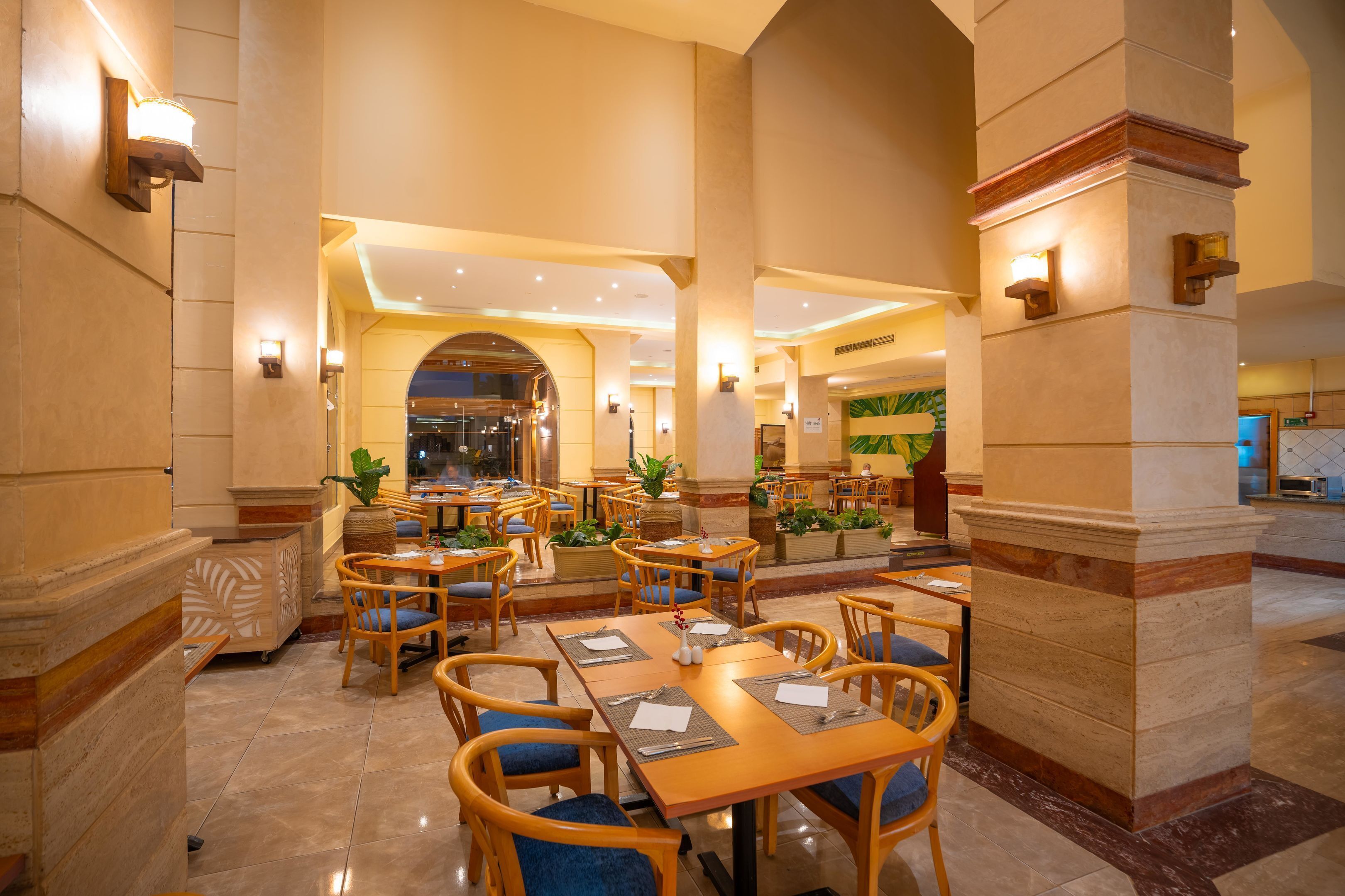 Un amplio vestíbulo de hotel con varias mesas y sillas de comedor, una zona de recepción y un gran arco que conduce a otra sección.