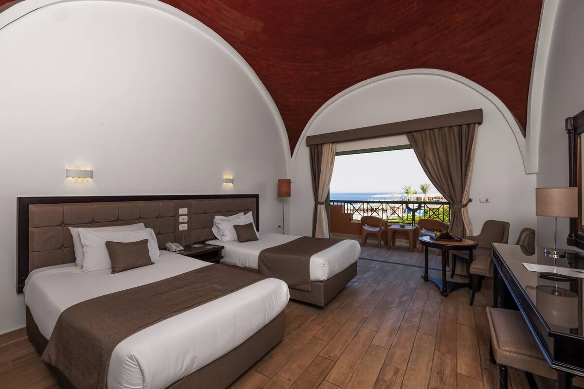 A hotel room with two beds, a desk, and a balcony with a view.