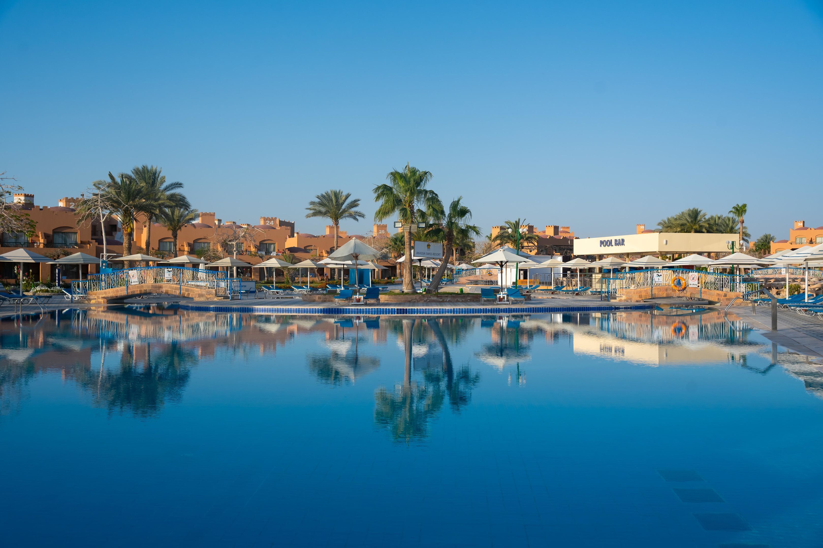 Zwembadterrein van een resort met ligbedden, parasols en palmbomen.