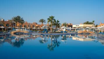 Zwembadterrein van een resort met ligbedden, parasols en palmbomen.