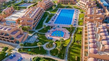 Ein Luftbild eines Resorts mit mehreren Gebäuden, einem großen zentralen Pool und umliegenden, angelegten Grünflächen.