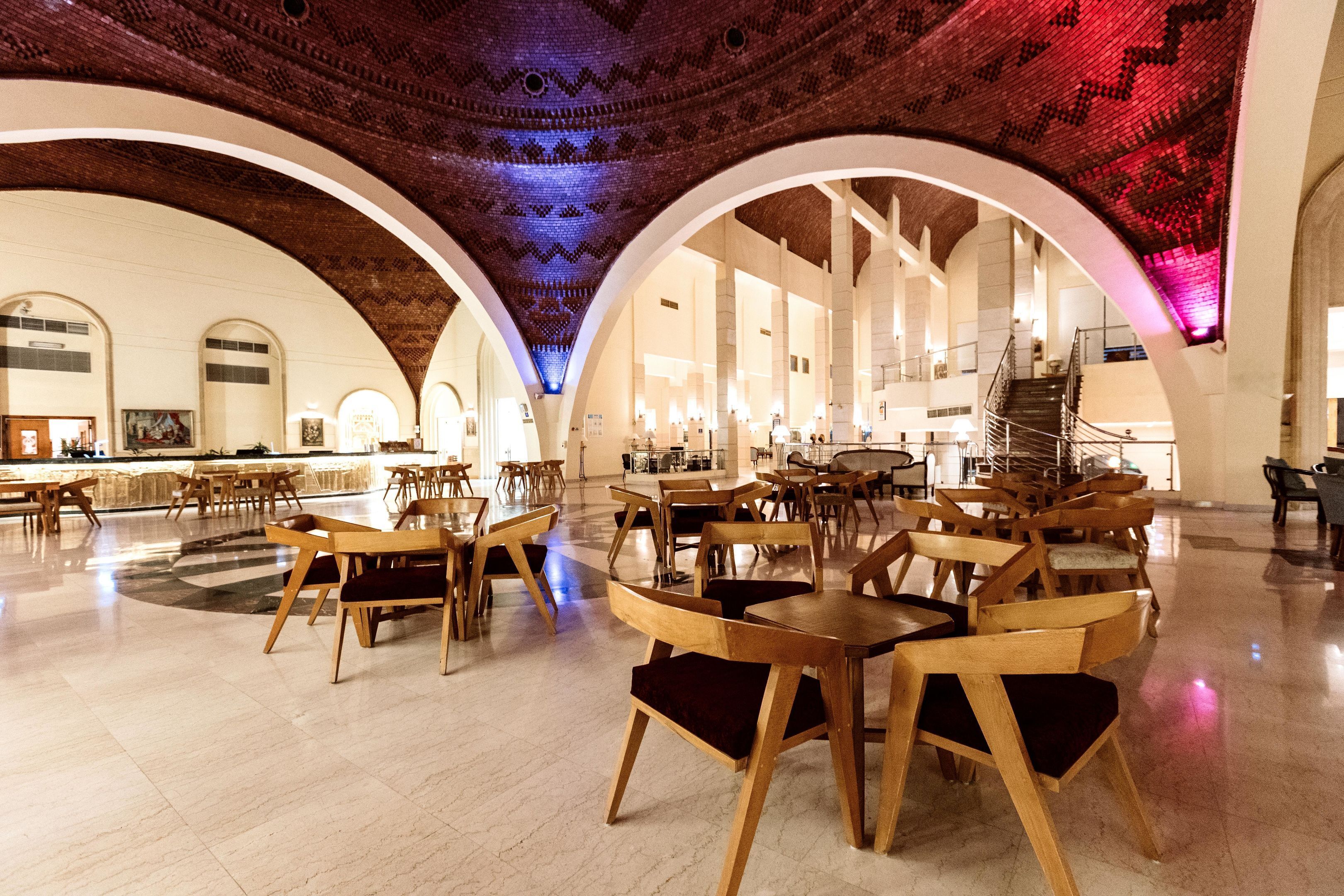 A spacious interior with high ceilings, arched ceilings, and a central staircase. Tables and chairs are arranged in a dining area.