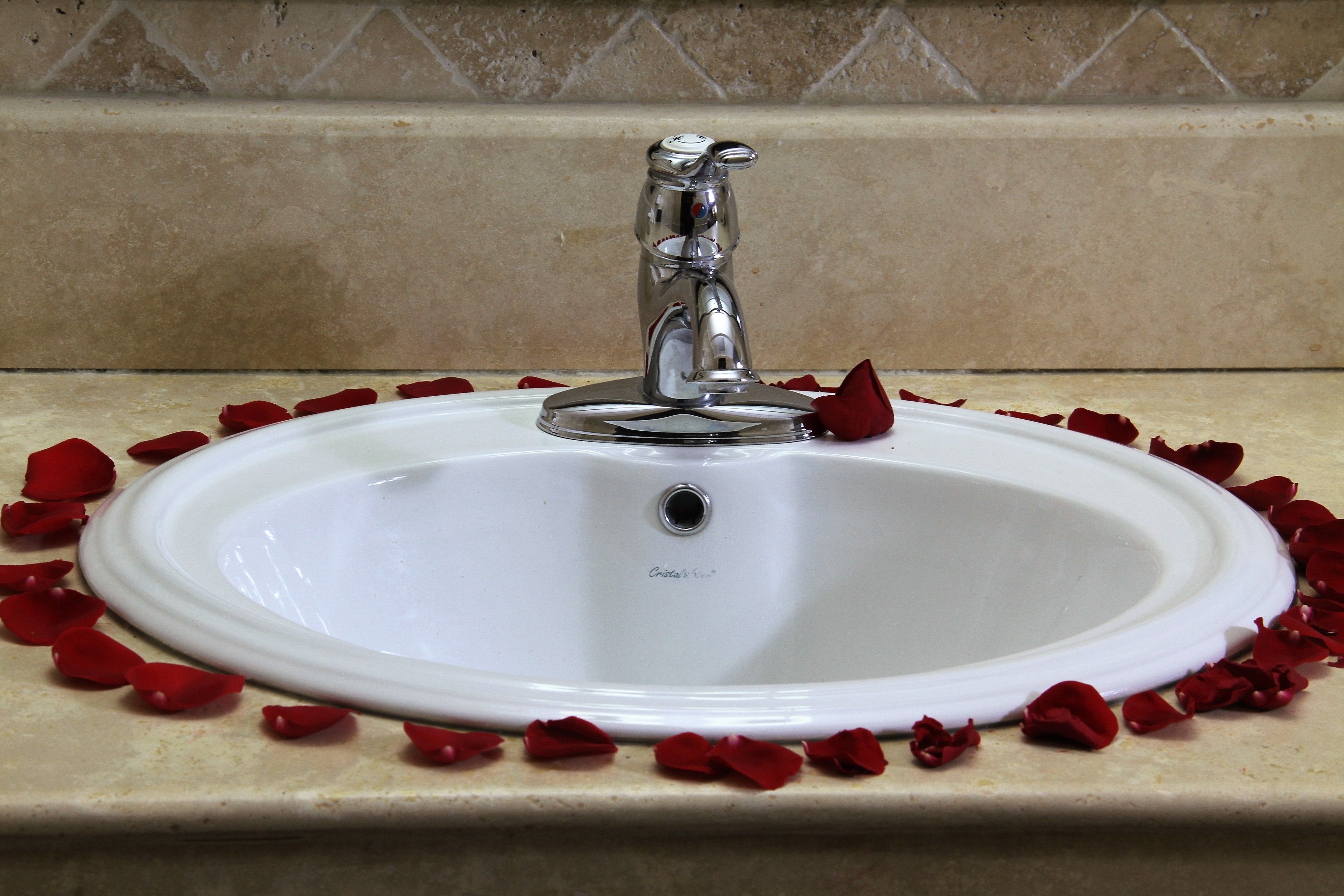 A white bathroom sink with a single faucet, surrounded by scattered rose petals.