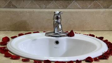 A white bathroom sink with a single faucet, surrounded by scattered rose petals.