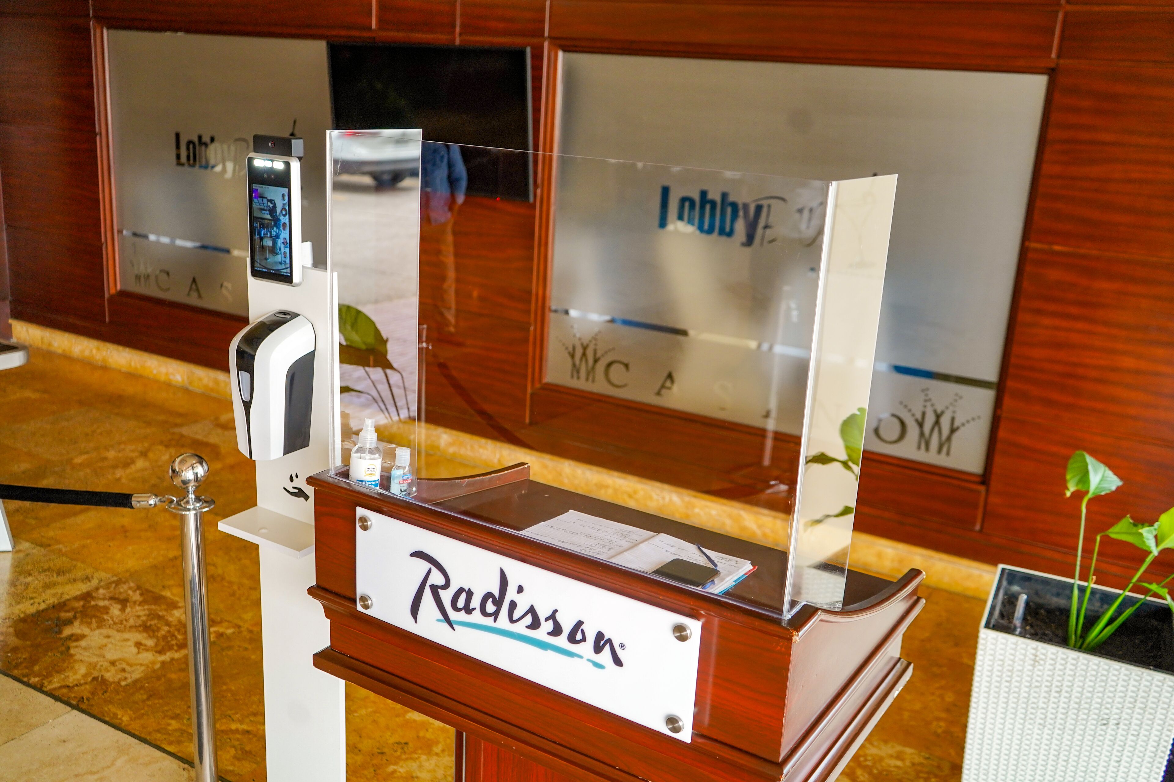 A reception desk with a nameplate reading "Radisson" and a digital kiosk.