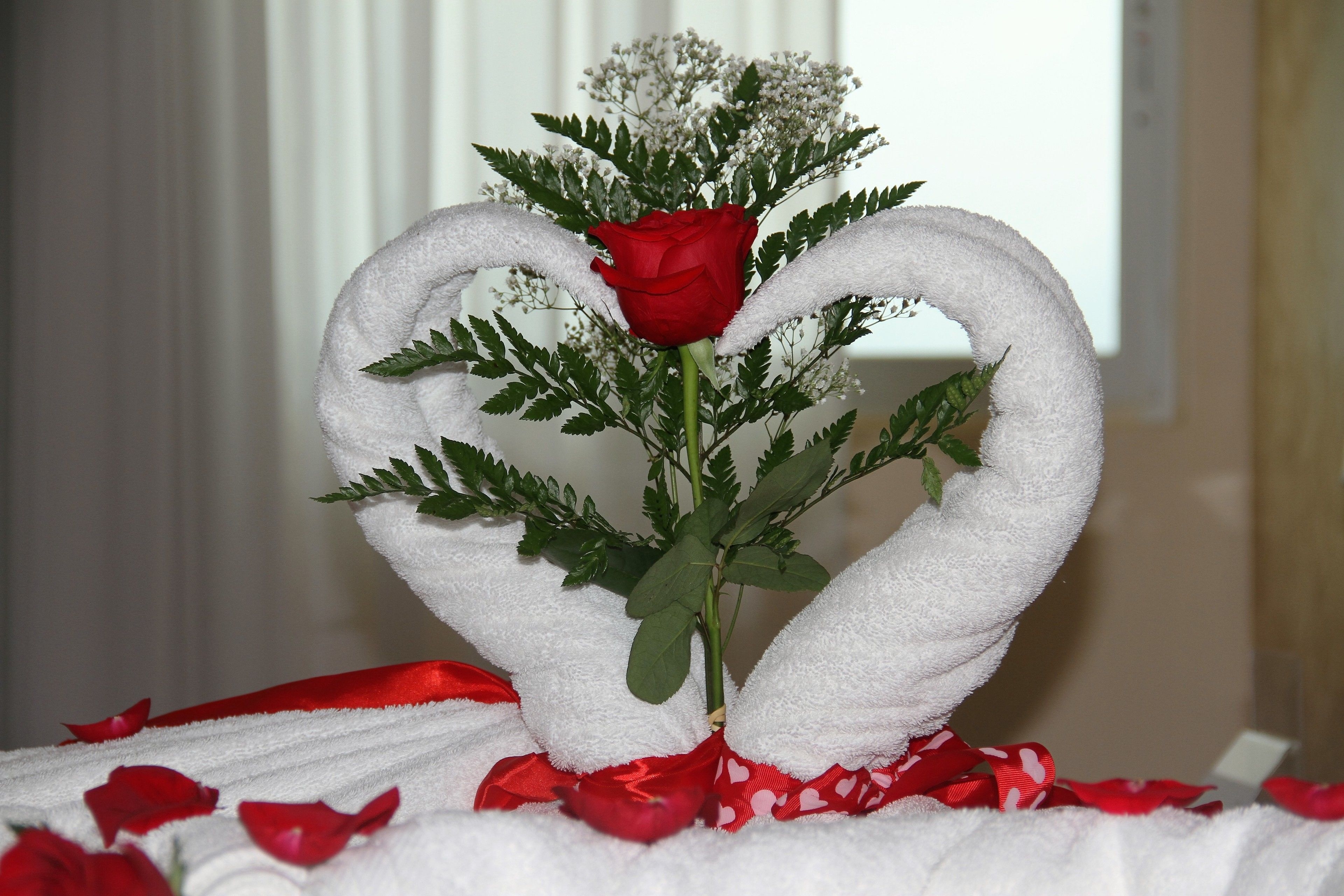 A decorative arrangement with a red rose and white towels shaped like swans.
