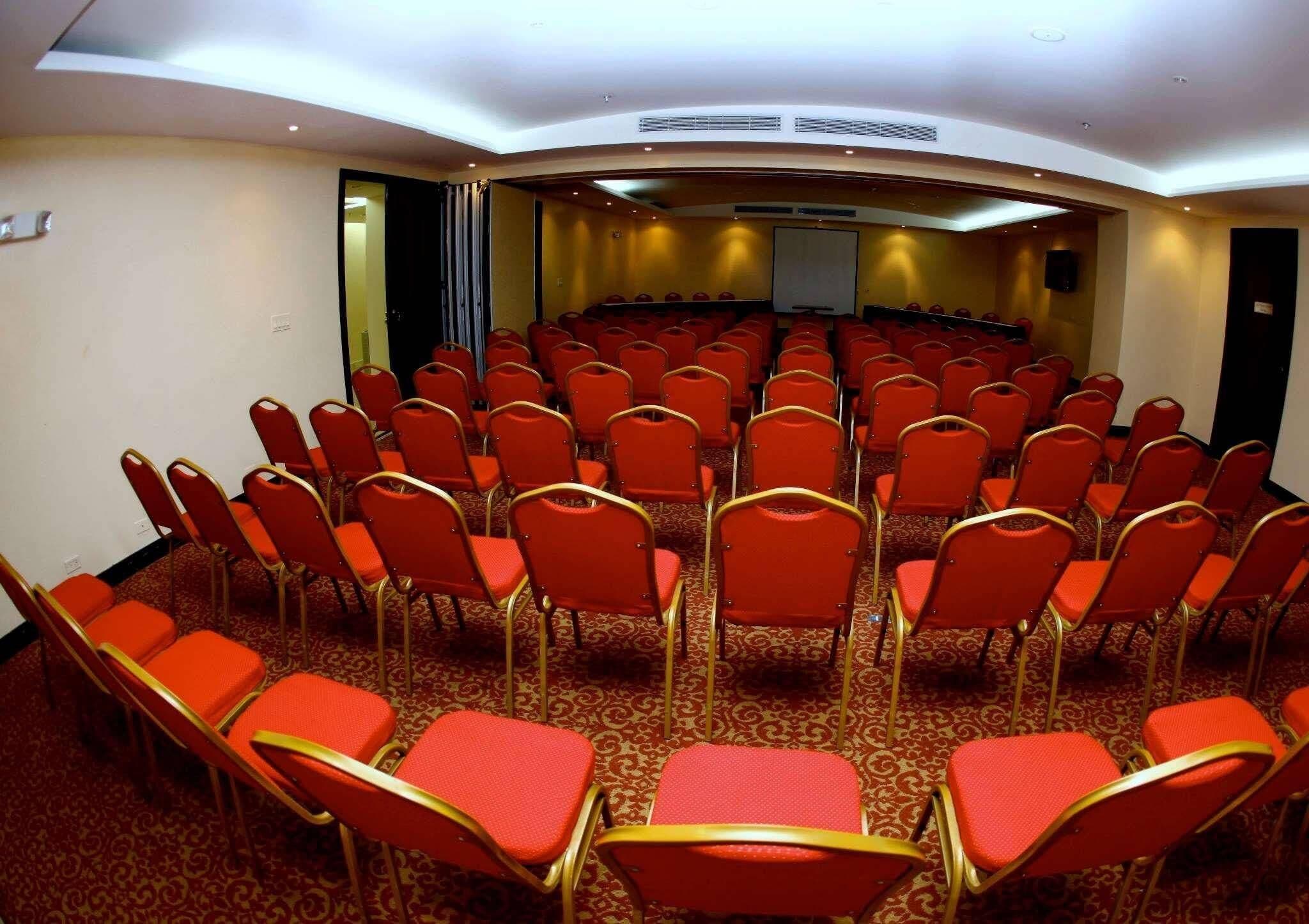 A conference room with rows of red chairs and a carpeted floor.