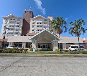 A hotel with a central entrance, multiple balconies, and palm trees.