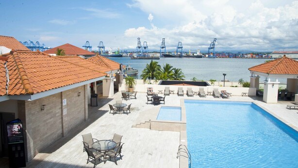 A rooftop pool area with lounge chairs and a view of a port with cranes. - Radisson Colon 2000 Hotel & Casino at Cruise Port & Duty Free Mall (Colon)