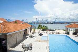 A rooftop pool area with lounge chairs and a view of a port with cranes.